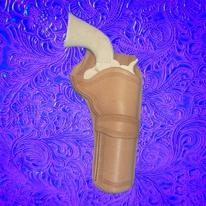 May include: A brown leather holster for a silver revolver. The holster has a stitched design and is on a purple background with a floral pattern.