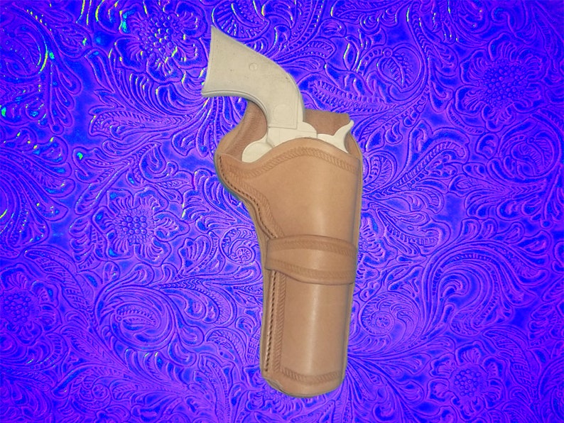 May include: A brown leather holster for a silver revolver. The holster has a stitched design and is on a purple background with a floral pattern.