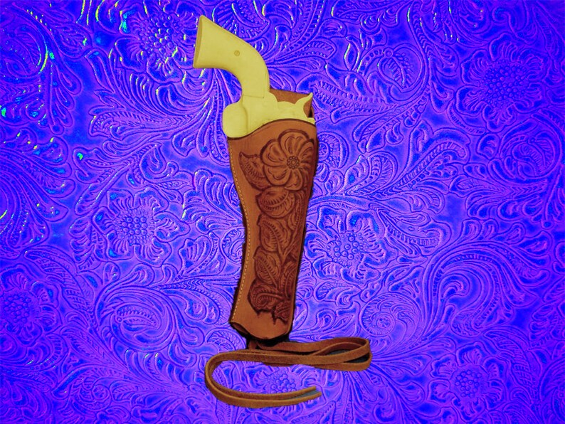 May include: A brown leather holster with floral embroidery, designed to hold a pistol. The holster is on a purple background with a floral pattern.