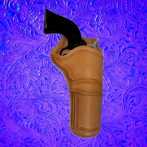 May include: A brown leather holster for a handgun. The holster has a stitched design and is shown against a purple background with a floral pattern.