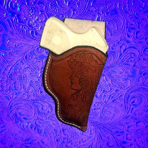 Pu&ograve; includere: Un fodero in pelle marrone con un motivo floreale e un contorno bianco. Il fodero &egrave; progettato per contenere una piccola pistola.