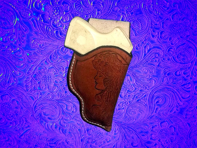 Pu&ograve; includere: Un fodero in pelle marrone con un motivo floreale e un contorno bianco. Il fodero &egrave; progettato per contenere una piccola pistola.