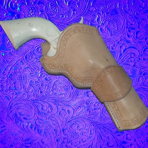 May include: A brown leather holster with intricate stitching and a white pistol inside. The holster is on a purple and blue patterned background.