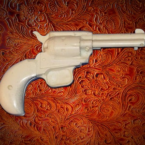 Puede incluir: Una pistola de juguete de plástico blanco sobre un fondo de cuero marrón.