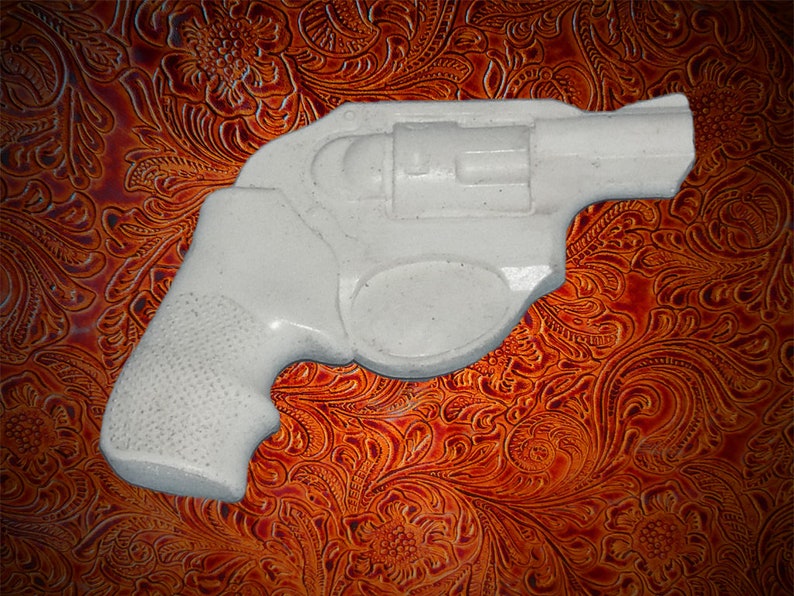 May include: A white plastic toy gun shaped like a revolver. The gun is on a brown patterned surface.
