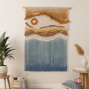 May include: A large macrame wall hanging featuring a landscape design. The artwork incorporates shades of brown, tan, and blue, with a sun motif. The piece is mounted on a wooden dowel, creating a textured, artistic wall decor.