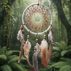 May include: A handmade dreamcatcher with a white and brown woven web design. It features wooden beads and decorative feathers in brown, tan, and white. The background is a blurred forest scene.