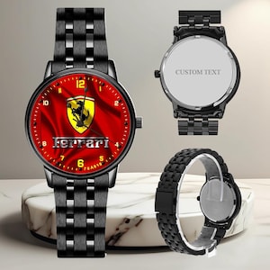 May include: Black wristwatch with a red face featuring the Ferrari logo and text. The watch has a black metal band and a round face. The image shows the front and back of the watch, and a separate band.