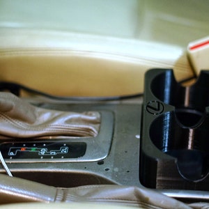 May include: A black plastic cup holder with the Lexus logo on the front. The cup holder is installed in a car's center console.