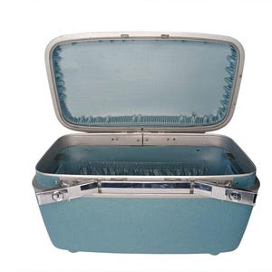 May include: A light blue hardshell vanity case with a textured exterior and a silver-toned metal frame. The interior is lined with matching light blue fabric, featuring gathered pockets along the sides and a hinged lid with a silver latch.