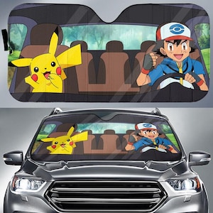 May include: Car windshield sunshade featuring Pikachu and Ash from the Pokémon anime. The sunshade has a black mesh background with a colorful illustration of the characters inside a car. The sunshade is designed to fit most car windshields.