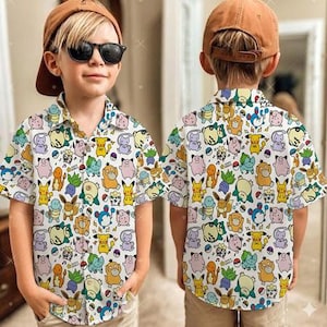 Może przedstawiać: Biała koszula zapinana na guziki z kolorowym wzorem postaci z kreskówek. Koszula ma krótkie rękawy i kołnierzyk. Koszula jest noszona przez młodą osobę noszącą okulary przeciwsłoneczne i brązową czapkę z daszkiem.