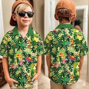 Peut inclure: Une chemise à manches courtes avec un col vert et un imprimé tropical vibrant avec des personnages de dessins animés et de grandes feuilles vertes. La chemise est principalement jaune et verte, avec une casquette de baseball marron.
