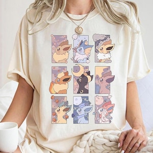 May include: A cream-coloured t-shirt displaying nine colourful illustrations of cartoon creatures within rectangular frames. The creatures are of various colours and designs, set against different coloured and patterned backgrounds. The shirt has short sleeves and a relaxed fit.