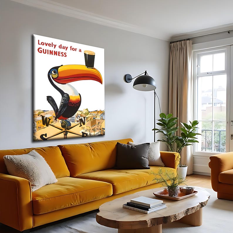May include: A framed Guinness advertisement featuring a toucan holding a pint of Guinness. The toucan has a large orange and yellow beak, with the text "Lovely day for a Guinness" in red. The artwork is displayed above a mustard yellow sofa.