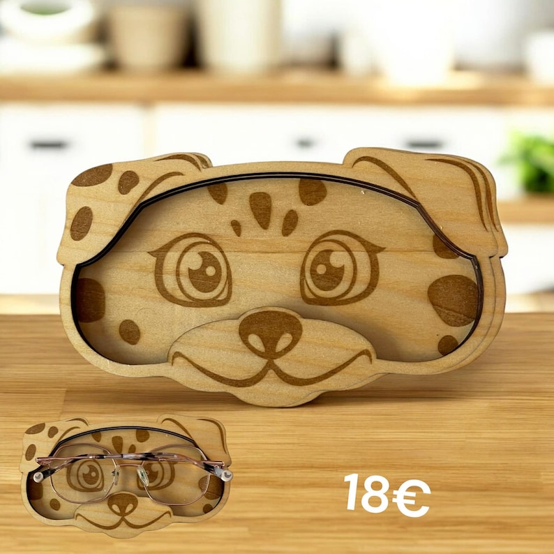 Puede incluir: Un estuche de madera para gafas con forma de cara de perro, con ojos, nariz y manchas grabadas. El soporte es de color marr&oacute;n claro con contornos y manchas marrones oscuras. Las gafas son visibles en el interior.
