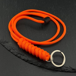 May include: A bright orange paracord lanyard featuring a tightly woven cobra knot section and a silver-toned metal split ring at one end. The cord is secured with a small black cylindrical bead, creating a continuous loop design for keys.