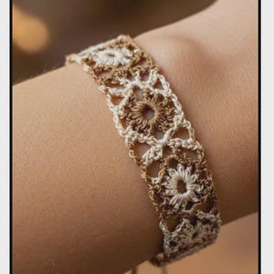 May include: A handmade crocheted bracelet in cream and brown. The bracelet has an openwork design with floral motifs. The close-up shows the intricate details of the crochet work. The bracelet is likely made of cotton yarn.
