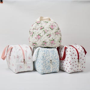 May include: Five quilted fabric bags in various floral and patterned designs. The bags feature different colors, including white with pink roses, white with pink butterflies, blue with small flowers, and white with red cherries. Each bag has a zipper closure and a handle.