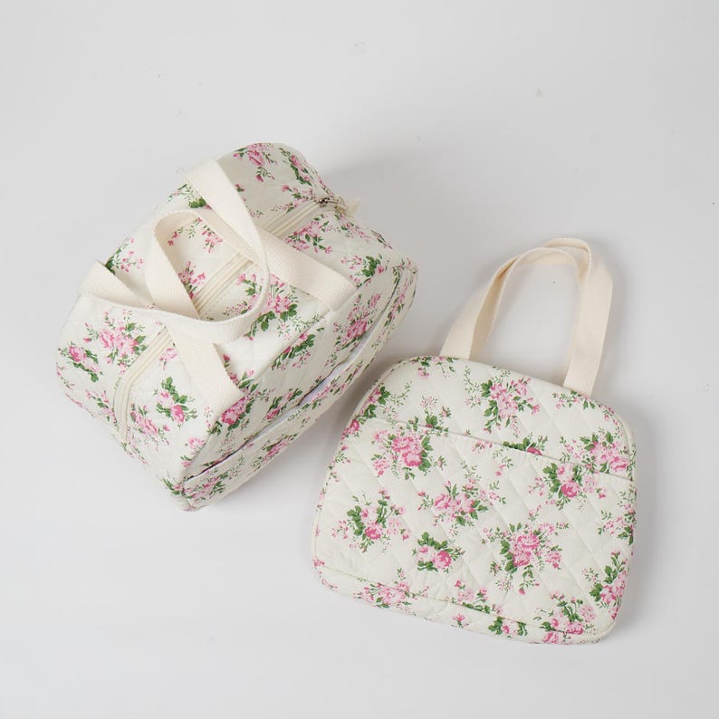 May include: Two quilted floral print bags. One is a rectangular duffel bag with cream-colored handles and a zipper closure. The other is a square tote bag with a cream-colored handle. Both bags feature a pattern of pink roses and green leaves on a cream background.