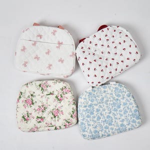May include: Four quilted fabric bags in various patterns. One bag features pink bows on a white background. Another has red cherries on white. The third has pink roses, and the fourth has blue floral patterns.