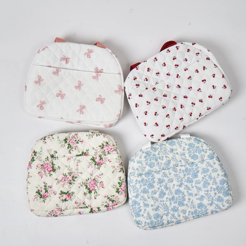 May include: Four quilted fabric bags in various patterns. One bag features pink bows on a white background. Another has red cherries on white. The third has pink roses, and the fourth has blue floral patterns.
