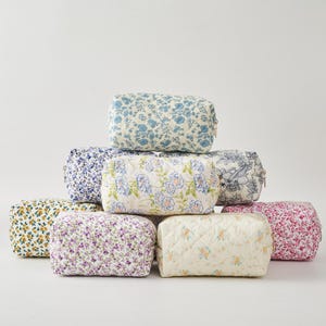 Puede incluir: Una colección de ocho neceseres con estampado floral en varios colores, incluyendo azul, amarillo, morado y rosa. Las bolsas son rectangulares con un diseño acolchado y cierre de cremallera. Las bolsas están apiladas unas sobre otras.