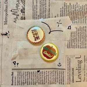 May include: Two round pinback buttons. One button has the text "29! 29! 29!" in a red and white design. The other button has a red apple graphic with the text "GAP TOOTH Smile!" in a yellow and green design.