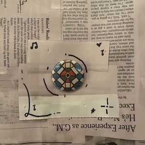 Peut inclure: Un bouton coloré avec un motif géométrique en mosaïque, composé de formes rouges, bleues, jaunes et vertes. Le bouton est placé sur un fond de coupures de journaux et de notes manuscrites.