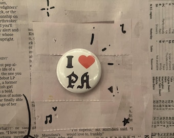 May include: A circular badge with "I PA" in black text and a red heart. It's set against a backdrop of newspaper cuttings and tape.