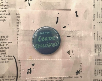 May include: A circular button, dark blue in colour, featuring the text "Did you... Leave Overjoyed?" in a light green, stylized font. The button is placed on a background of newspaper cuttings and handwritten symbols.