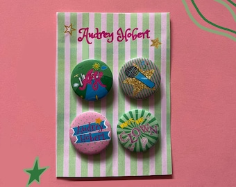 May include: A set of four circular pinback buttons attached to a light green and white striped display card with the text Audrey Hobert. The buttons feature colourful designs including a microphone, the name Audrey Hobert, and the text Who's the Clown.