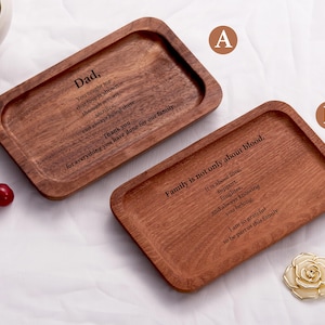 Puede incluir: Dos bandejas rectangulares de madera con bordes redondeados. Una bandeja está grabada con las palabras "Dad" y un mensaje de gratitud. La otra bandeja está grabada con las palabras "Family is not only about blood" y un mensaje. Una flor decorativa es visible.