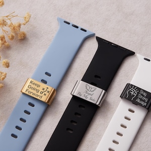 Puede incluir: Tres correas de Apple Watch en azul claro, negro y blanco. Cada correa presenta un cierre metálico con un mensaje grabado: "Keep Going Forward", "Angel By My Side" y "Stay Strong Always".