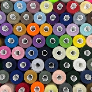 May include: A close-up of a selection of thread spools in various colours. The spools are arranged in a grid, displaying a range of hues such as red, yellow, green, blue, purple, and pink. The thread is neatly wound on each spool.