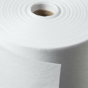 May include: A roll of white, non-woven fabric. The fabric is tightly wound around a cardboard core, with a small section of the fabric pulled away, revealing its texture. The image is a close-up, highlighting the fabric's smooth surface.