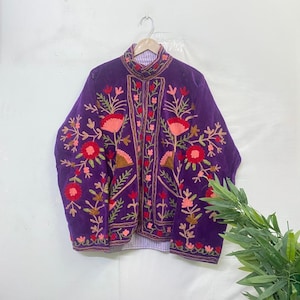 May include: A striking purple jacket adorned with detailed floral embroidery in red, pink, and green. The jacket has a high collar and a striped lining. The embroidery is intricate, covering the front and sleeves, creating a visually appealing garment.