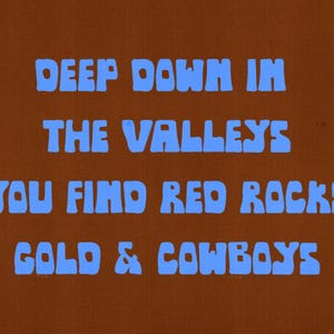 May include: A brown background with the blue text: "DEEP DOWN IN THE VALLEYS YOU FIND RED ROCKS GOLD & COWBOYS". The text is in a bold, rounded font. The overall design has a vintage, retro aesthetic.