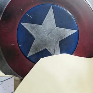 May include: A Captain America shield prop, featuring a blue central disc with a silver star, surrounded by concentric rings of silver, white, and red. The shield is a classic superhero accessory.