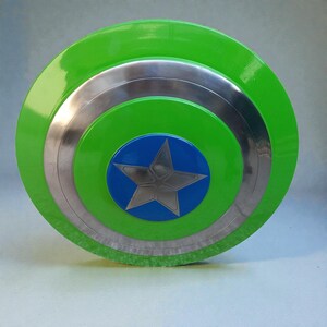 Pu&ograve; includere: Uno scudo rotondo con un anello esterno verde brillante, bande argentate e un centro blu. Una stella argentata &egrave; al centro del cerchio blu. Lo scudo ha una finitura lucida.
