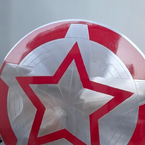 Peut inclure: Un bouclier rond avec un design rouge et argent&eacute;. Le bouclier pr&eacute;sente une grande &eacute;toile rouge au centre, entour&eacute;e de segments argent&eacute;s et d'une bordure rouge. Le bouclier a une finition brillante.