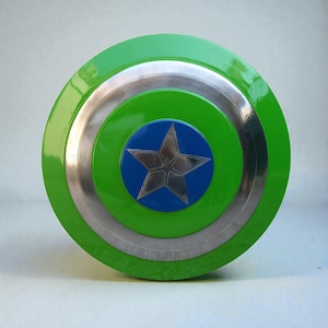 Pu&ograve; includere: Uno scudo rotondo con un anello esterno verde, un anello interno argentato e un centro blu. Una stella argentata &egrave; al centro del cerchio blu. Lo scudo &egrave; un oggetto di scena o un giocattolo.