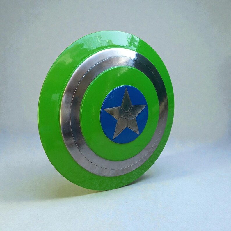Pu&ograve; includere: Uno scudo rotondo con un anello esterno verde, bande argentate e un centro blu. Una stella argentata &egrave; al centro del cerchio blu. Lo scudo ha una finitura lucida ed &egrave; probabilmente un accessorio di costume.