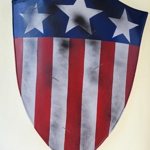May include: A shield with a blue top section featuring three white stars. The lower portion has red and white vertical stripes. The shield has a distressed, aged appearance.