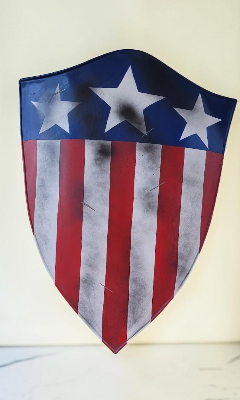 May include: A shield with a blue top section featuring three white stars. The lower portion has red and white vertical stripes. The shield has a distressed, aged appearance.