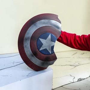 May include: A Captain America shield, featuring a blue central disc with a white star, surrounded by red and silver concentric rings. The shield is a prop, likely for cosplay or display.
