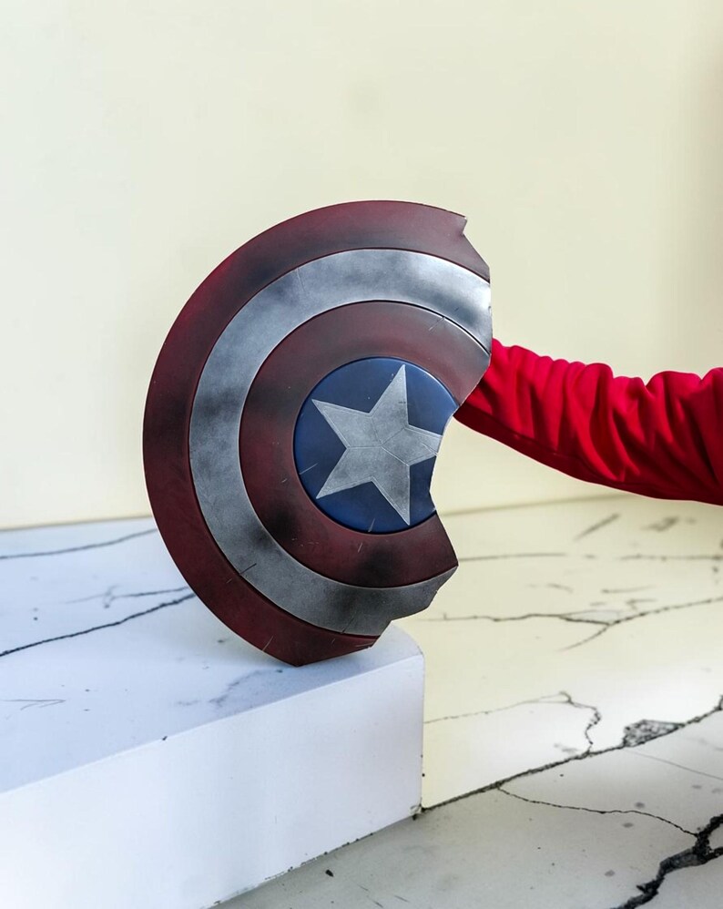 May include: A Captain America shield, featuring a blue central disc with a white star, surrounded by red and silver concentric rings. The shield is a prop, likely for cosplay or display.