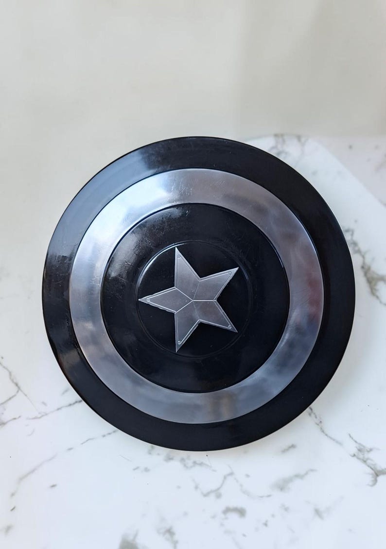 Op de afbeelding: Een zwart en zilver schild met een centraal zilveren sterembleem. Het schild heeft concentrische cirkelvormige banden van zwart en zilver. De ster is een vijfpuntig ontwerp. Het schild is een rekwisiet of verzamelobject.