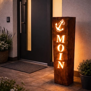 Könnte beinhalten: Eine rechteckige Außenleuchte aus verwittertem Metall mit Ankerdesign und dem Wort "MOIN" in Weiß beleuchtet. Die Leuchte steht auf einer gefliesten Terrasse in der Nähe einer Eingangstür und Topfpflanzen. Das Thema ist maritim.