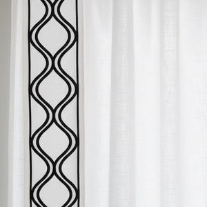 May include: White curtain panel with a black, wavy, geometric border design. The curtain hangs from a silver rod with metal rings. The design is a repeating pattern of interconnected, curved lines.